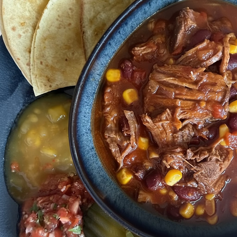 Bildet viser en blå tallerken med Tortillalefser,en mangosalsa, en tomatsalsa og tortillaschips. i midten såt en blå skål fylt med chili con carne som er rød og dyp i fargen, med kjøtt som smelter på tungen, maiskorn og bønner.